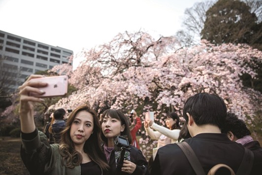 Women taking a selfie with cherry blossoms in a park in Tokyo.
