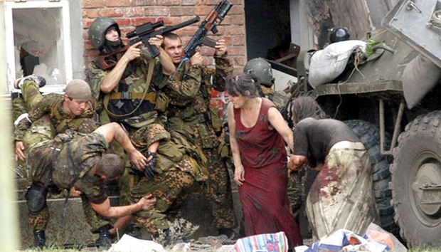 This file photo taken on September 3, 2004 shows a Russian special police soldier (left) carrying an injured colleague as two soldiers and two women take cover behind an armoured personnel carrier during the rescue operation of the school in Beslan, northern Ossetia.