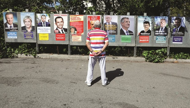 A man looks at campaign posters of the 11 candidates running in the 2017 French presidential election, in Saint Andre de La Roche, near Nice, France. From left, the candidates are Debout La France group candidate Nicolas Dupont-Aignan, Marine Le Pen, Emmanuel Macron, Benoit Hamon, Lutte Ouvriere political party leader Nathalie Arthaud, Anti-Capitalist Party presidential candidate Philippe Poutou, Solidarite et Progres (Solidarity and Progress) party candidate Jacques Cheminade, lawmaker and independent candidate Jean Lassalle, Jean-Luc Melenchon, UPR candidate Francois Asselineau, and Francois Fillon.