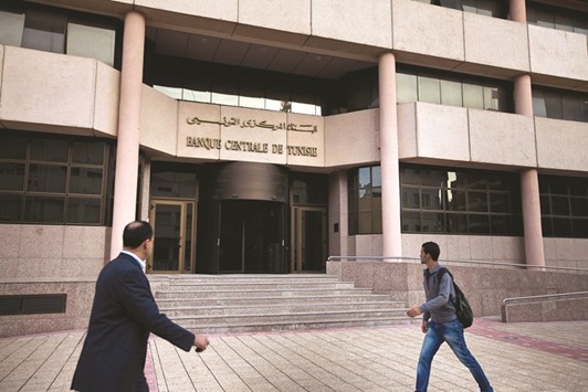 Pedestrians pass the headquarters of the Tunisian central bank in Tunis. The bank will reduce interventions so the value of the dinar gradually declines though it will prevent a dramatic slide in the currency, the finance minister said yesterday.