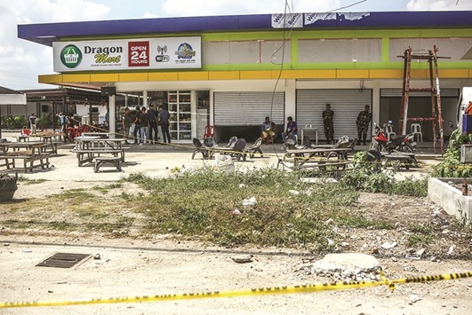 Police and military personnel stand near the site where two bombs exploded on Monday, at a gasoline in Tacurong town, Sultan Kudarat province, in southern island of Mindanao yesterday.