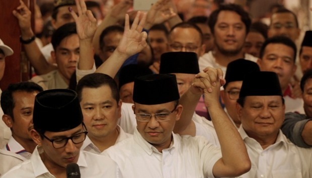 Former Indonesian education minister Anies Baswedan (C) holds the hand of Gerindra party chief Prabowo Subianto (R) as Baswedan running mate Sandiaga Uno (L) talks to reporters after voting in the Jakarta governor election in Jakarta.