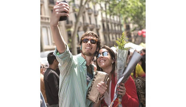 A couple holding a rose and a book take a selfie on the Ramblas of Barcelona on Saint Georgeu2019s Day. Traditionally, a man gives a woman a rose and the woman gives the man a book to celebrate the Catalan holiday also known as u2018The Day of the Roseu2019 or u2018The Day of the Booku2019