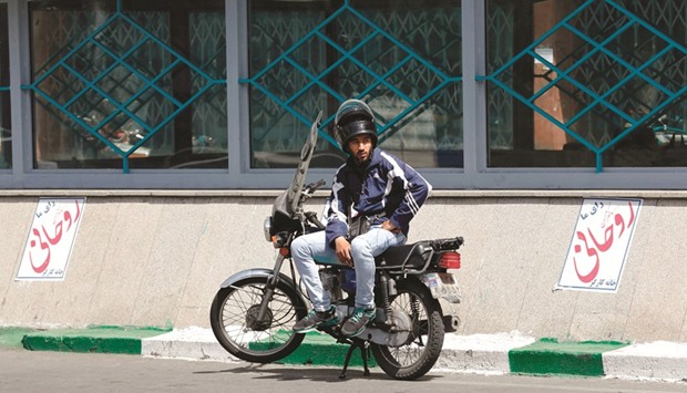An Iranian man sits on a motorcycle between election posters of President Hassan Rouhani, who is running for the presidential elections, in Tehran yesterday.