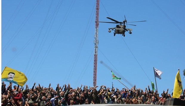 Kurds wave flags as a medical helicopter, from the US-led coalition, flies over the site of Turkish airstrikes near northeastern Syrian Kurdish town of Derik.