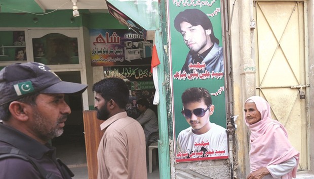 A policeman (left) and residents walk past a shop displaying the pictures of men, who were killed in a suicide blast on January 2015, in a Shia mosque at Shikarpur, Pakistan on March 19, 2017.