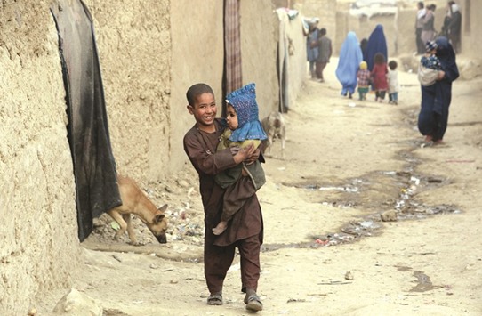 This file photo taken on December 16, 2016 shows an internally displaced Afghan boy holding a child as he walks outside his temporary home at a refugee camp in Kabul.