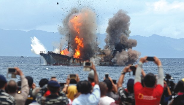 People take pictures of a burning ship as the government destroyed foreign boats that had been caught illegally fishing in Indonesia waters, at Morela village in Ambon island.