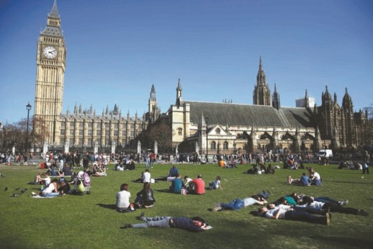 People relax in the sunshine in Parliament Square in front of the Houses of Parliament in central London.
