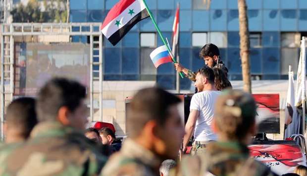 A Syrian soldier waves Russian and Syrian flags during a protest against air strikes in Damascus