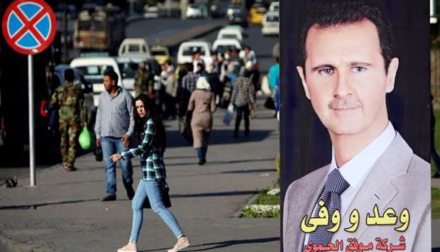 A woman walks near a picture of Syrian President Bashar al Assad in Damascus.