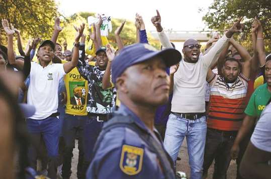 A police officer looks on as protesters chant slogans during protests in Mahikeng, in the North West province, South Africa, yesterday.