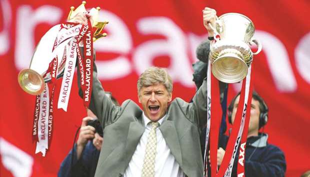 In this file photo, Arsenal Manager Arsene Wenger celebrates by holding aloft the FA Cup and Championship trophy during a victory parade in London on May 12, 2002. (Reuters)