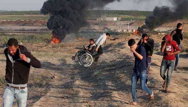 A wheelchair-bound Palestinian photographer is helped, as others react from tear gas fired by Israeli troops at a protest at the Israel-Gaza border where demonstrators demanded the right of Palestinians to return to their homeland, east of Gaza City on Sunday.