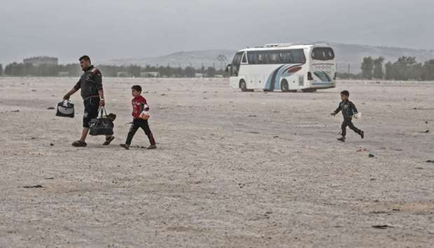Members of a Syrian family evacuated from the town of Dumayr, east of the capital Damascus, carry their belongings as they walk away after disembarking from their bus in the city of Azaz in the northern countryside of Aleppo  yesterday.