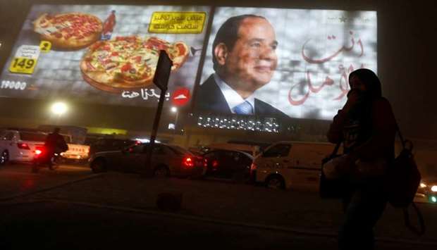 Woman walks past a billboard showing a picture of Egyptian President Abdel Fattah al-Sisi during a sandstorm in Cairo