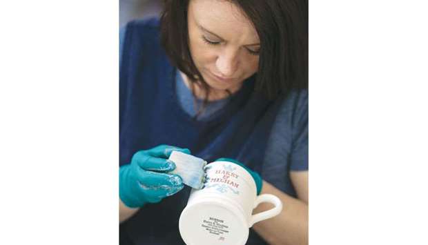 A worker hand-paints a commemorative mug, with a message celebrating the forthcoming wedding of Prince Harry and his US fiance Meghan Markle, at the Emma Bridgewater factory in Stoke-on-Trent, central England.