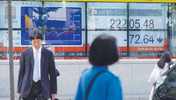 Pedestrians walk past a stock indicator showing share prices of the Tokyo Stock Exchange. The index closed 0.3 % lower at 22,215.32 points yesterday.