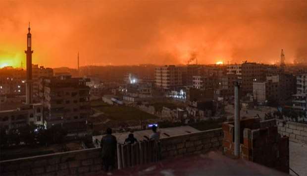 People stand on a roof to observe explosions in the skyline of a southern district of the Syrian capital Damascus