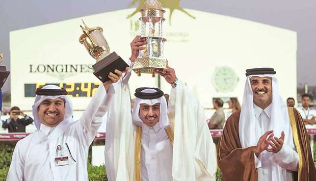 In this February 24, 2018, picture, His Highness the Amir Sheikh Tamim bin Hamad al-Thani applauds as The Blue Eyeu2019s owner Khalifa bin Sheail al-Kuwari (centre) and trainer Jassim Mohamed Ghazali (left) lift their trophies after the six-year-old won HH The Amiru2019s Trophy (Gr1) at the Qatar Racing and Equestrian Club.