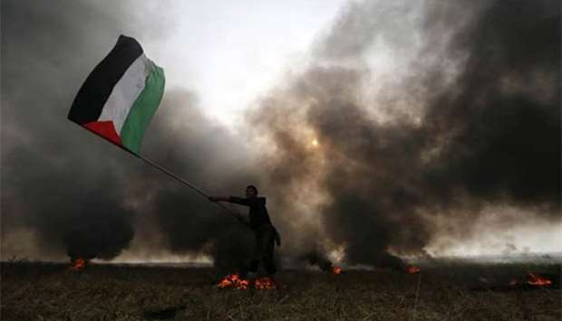 A protester waves a Palestinian flag as smoke rises from burning tyres during clashes with Israeli troops at Israel-Gaza border in the southern Gaza Strip on Thursday.