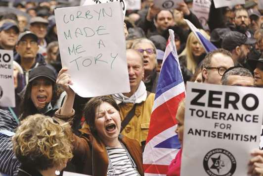 A woman holds up a placard declaring u201cCorbyn made me a Toryu201d as she joins protesters gathering for a demonstration organised by the Campaign Against Anti-Semitism outside the head office of the Labour Party in central London yesterday.