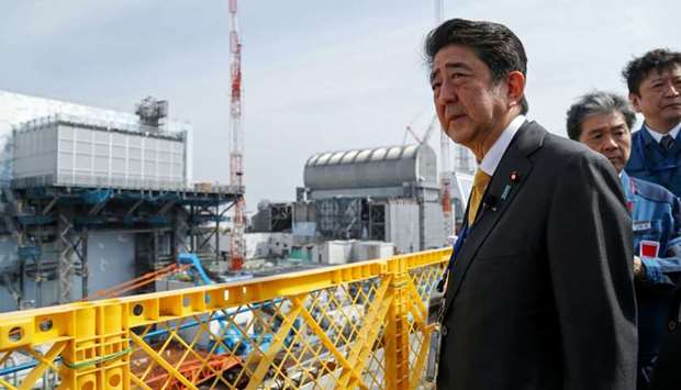 In this picture taken on April 14, 2019 Japan's Prime Minister Shinzo Abe visits the Tokyo Electric Power Company's (TEPCO) Fukushima Dai-ichi nuclear power plant as he stands in front of the reactor number 2 (L) and number 3 (R) buildings in Okuma, Fukushima prefecture
