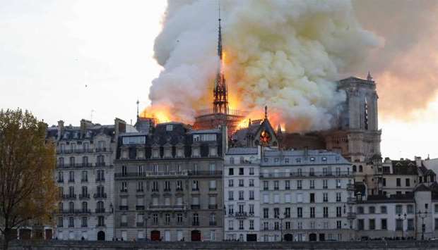 Seen from across the Seine River, smoke and flames rise during a fire at the landmark Notre-Dame Cathedral in central Paris
