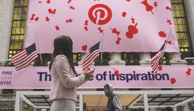 A woman uses her phone as a banner celebrating the IPO of Pinterest Inc hangs on the front of the New York Stock Exchange.