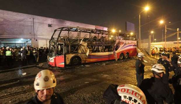 Police officers stand around the charred remains of a bus that caught fire in an interprovincial bus station in a populous district north of Lima