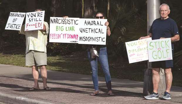 Protestors hold signs yesterday as the motorcade of President Donald Trump makes its way to his golf club in West Palm Beach, Florida.