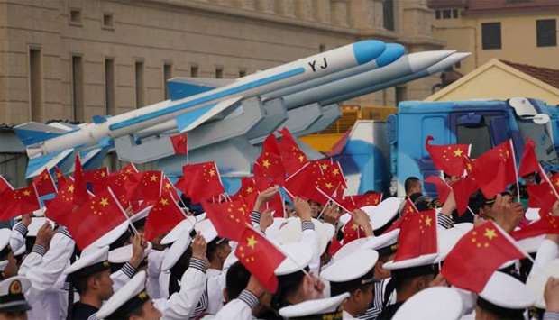 Chinese People's Liberation Army (PLA) Navy soldiers wave Chinese flags next to a model of a military vehicle carrying anti-ship missiles