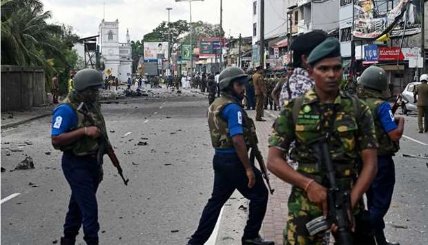 Sri Lankan soldiers stand guard as security personnel inspect the debris of a car after it explodes when police tried to defuse a bomb