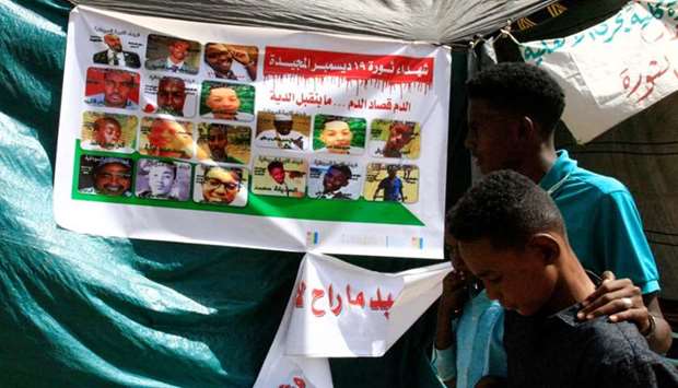 Sudanese protesters walk past a banner bearing the portraits of protesters, who died during the deadly crackdown on protests that erupted in December in response to Bashir government's decision to triple the price of bread, outside the army headquarters in the capital Khartoum. AFP