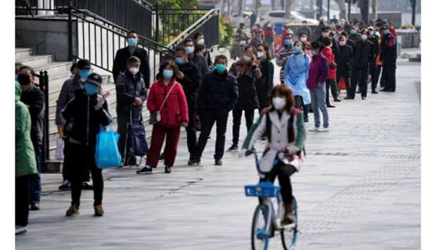 A woman wearing a face mask rides a shared bicycle past people lining up to enter a supermarket in Wuhan, Hubei province, the epicentre of Chinau2019s coronavirus disease (Covid-19) outbreak, yesterday.
