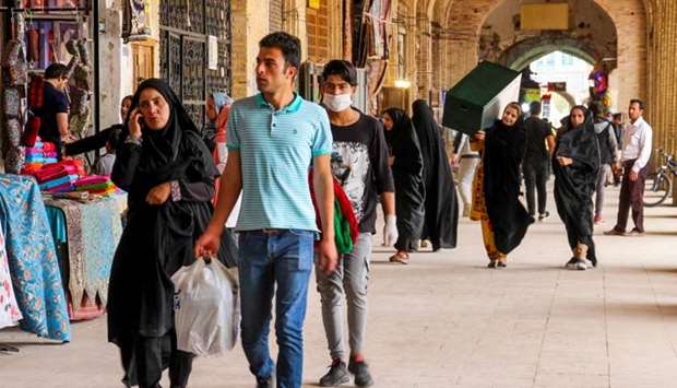 Iranians, some wearing personal protective equipment, walk past shops in the southeastern city of Kerman on April 11