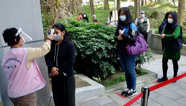 A masked local resident (2nd L) has her temperature checked as people line up to buy face masks from vending machines at the Xinyi District Health Center in Taipei. AFP