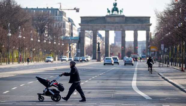 A woman pushing a pram crosses an almost deserted 17th June street near Brandenburger gate in Berlin yesterday as Germany continues its battle against the Covid-19 corona virus. The avenue leading up to the landmark Brandenburger Gate is normally one of the busiest stretches of road in the German capital but are now largely empty as people work from home.