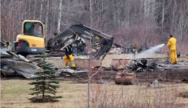 Volunteer firefighters douse hotspots as an excavator digs through the rubble of a destroyed home linked to Sundayu2019s deadly shooting rampage in Wentworth Centre, Nova Scotia, Canada.
