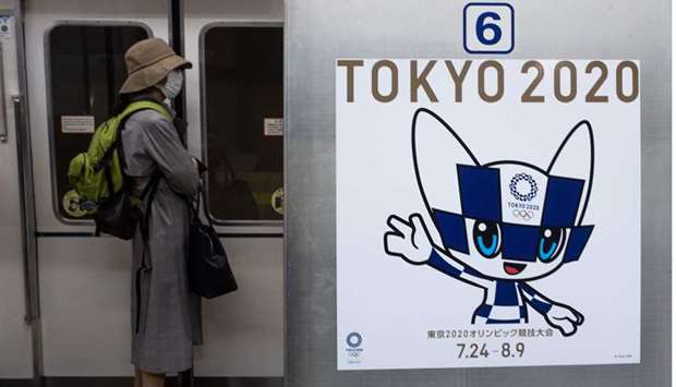 A passenger wearing a face mask stands next to a poster of Tokyo 2020 Olympic mascot Miraitowa on a train in Tokyo, Japan, yesterday. (AFP)