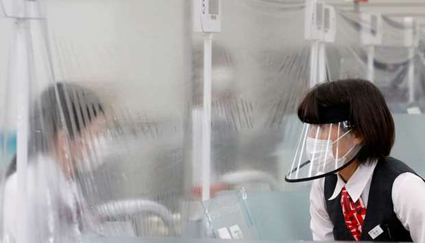A staff member wearing a face shield talks to a bank teller at a counter where a plastic curtain is installed in order to prevent infections following the coronavirus disease outbreak, at the Higashinakano branch of MUFG Bank in Tokyo, Japan.
