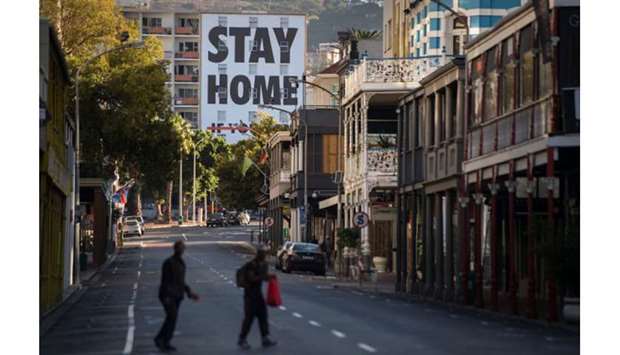Two men walk across Long Street, usually one of the busiest and most popular entertainment areas with bars, clubs and restaurants in the city, with a billboard reading Stay Home, in Cape Town, yesterday.