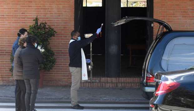 Roberto, a Congolese student priest, sprinkles holy water on the coffin of a Covid-19 coronavirus victim inside a hearse at a cemetery in Madrid