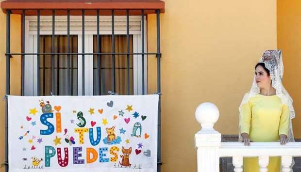 A girl wearing a traditional mantilla dress stands next to a banner as she celebrates Palm Sunday outside their house during lockdown, amid the coronavirus disease (Covid-19) outbreak, in Ronda, southern Spain. The banner reads: ,Yes, you can,.