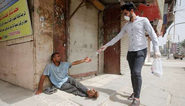 An Iraqi man wearing a protective face mask and gloves gives a bottle of water to a homeless man, who sits in front of a closed shop during a curfew imposed to prevent the spread of coronavirus disease (Covid-19), in Basra, Iraq