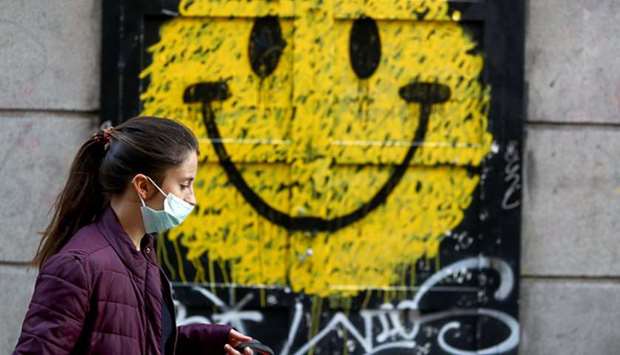 A woman walks past a closed shop in Madrid with a smiley painted on its door.
