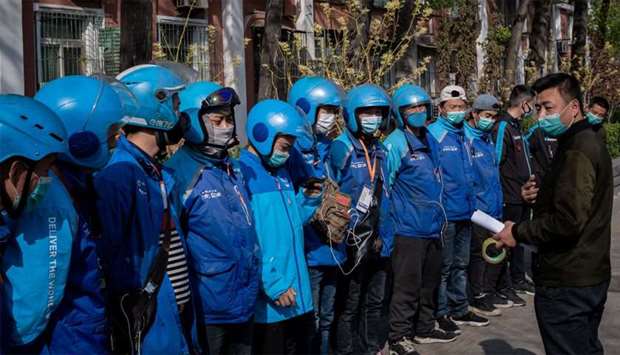 Delivery workers (L) wearing face masks amid the COVID-19 coronavirus pandemic listen to instructions for their daily work shift in Beijing