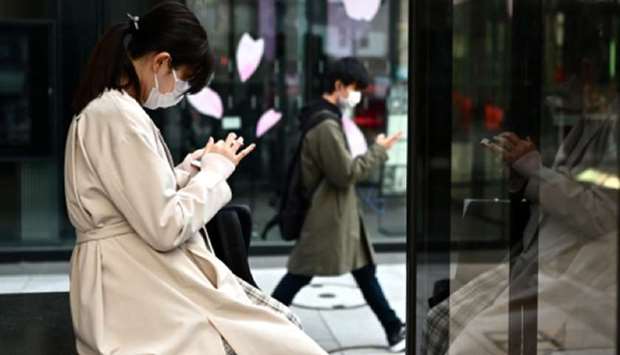 A woman wearing a face mask, amid concerns of the coronavirus outbreak, uses her phone on a street in Tokyo yesterday.