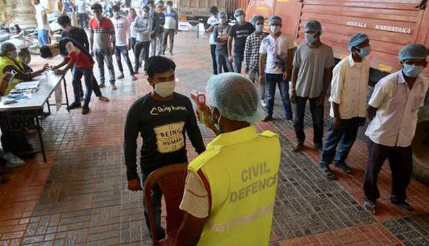 A volunteer gets his temperature checked as others sign-up and stand in a queue before entering a warehouse to pack emergency essentials and groceries to be distributed to people in Bengaluru yesterday.