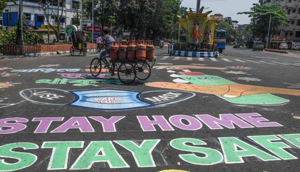 A man rides a three-wheeler cart loaded with gas cylinders as he crosses a road covered with paintings about precautions to follow during a government-imposed nationwide lockdown, in Kolkata yesterday.